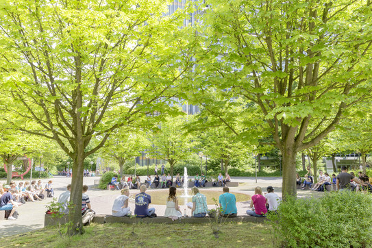 Studierende sitzend am Springbrunnen auf dem Campus Nord im Sommer