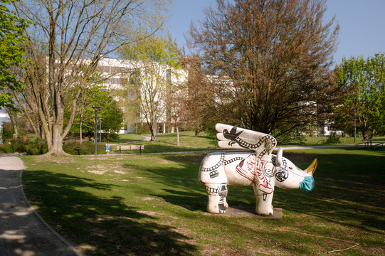 Eine grüne Anlage am Campus mit grünen Bäumen und eine Nashornfigur steht auf einer Wiese.