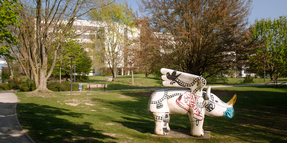 A green area at the campus with green trees and a rhinoceros figure stands on a meadow.